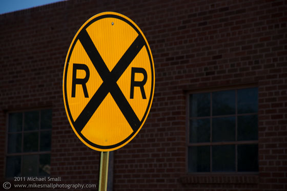 Photo of a railroad crossing sign against an old brick warehouse in Tucson, AZ